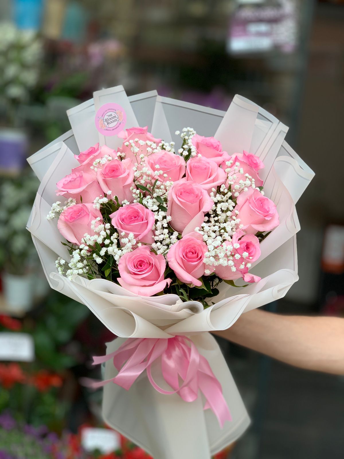 Buchet romantic cu 15 trandafiri roz proaspeți și gypsophila albă&nbsp;și pistachio verde, înfășurat elegant în hârtie crem cu fundă roz.